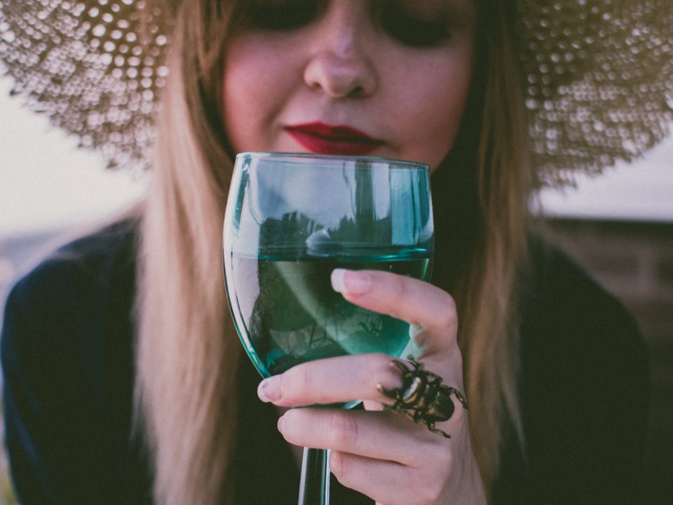 Junge Dame mit einem Strohhut hat ein gefülltes Glas vor sich und riecht daran