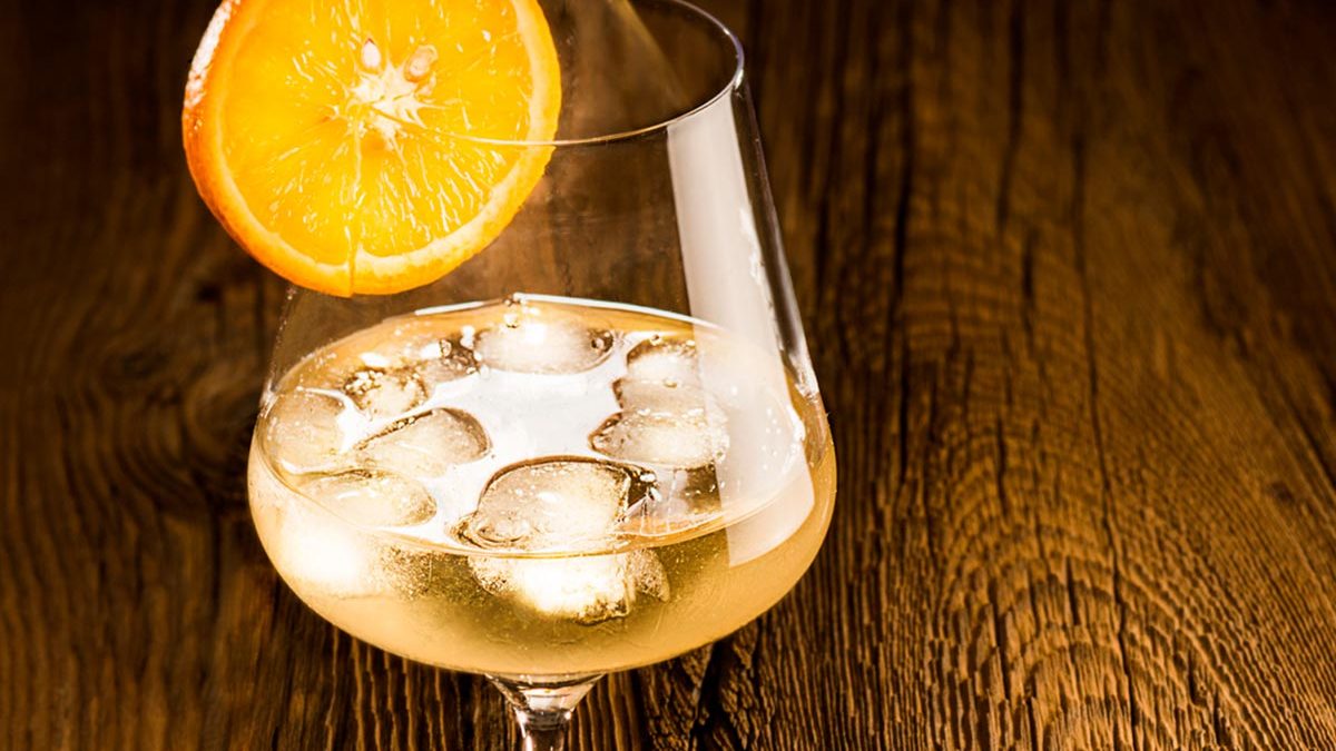 Vermouth 700 mit Eiswürfeln in einem Weinglas. Orangenscheibe als Dekoration, Holz als Hintergrund
