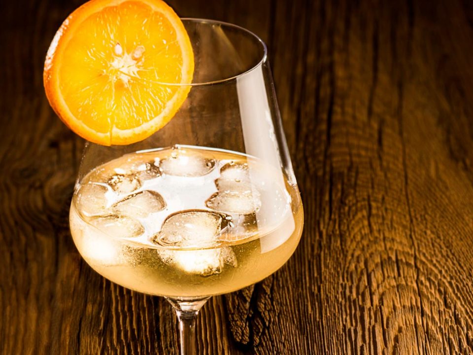 Vermouth 700 mit Eiswürfeln in einem Weinglas. Orangenscheibe als Dekoration, Holz als Hintergrund