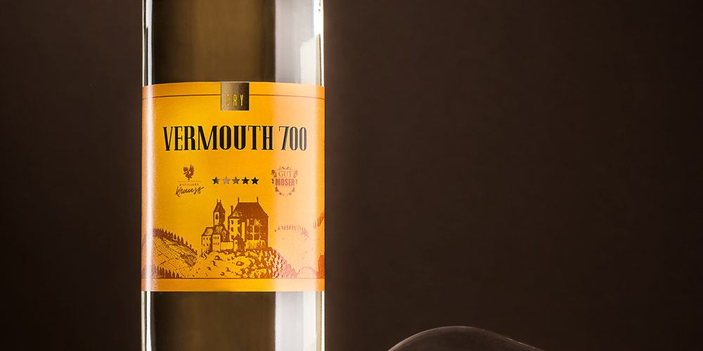 hohe, schlanke 750ml-Flasche gefüllt mit weißem Wermut. Dunkler Hintergrund, liegendes, leeres Weinglas als Dekoration, Vermouth 700