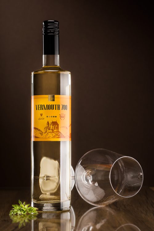 hohe, schlanke 750ml-Flasche gefüllt mit weißem Wermut. Dunkler Hintergrund, liegendes, leeres Weinglas als Dekoration, Vermouth 700